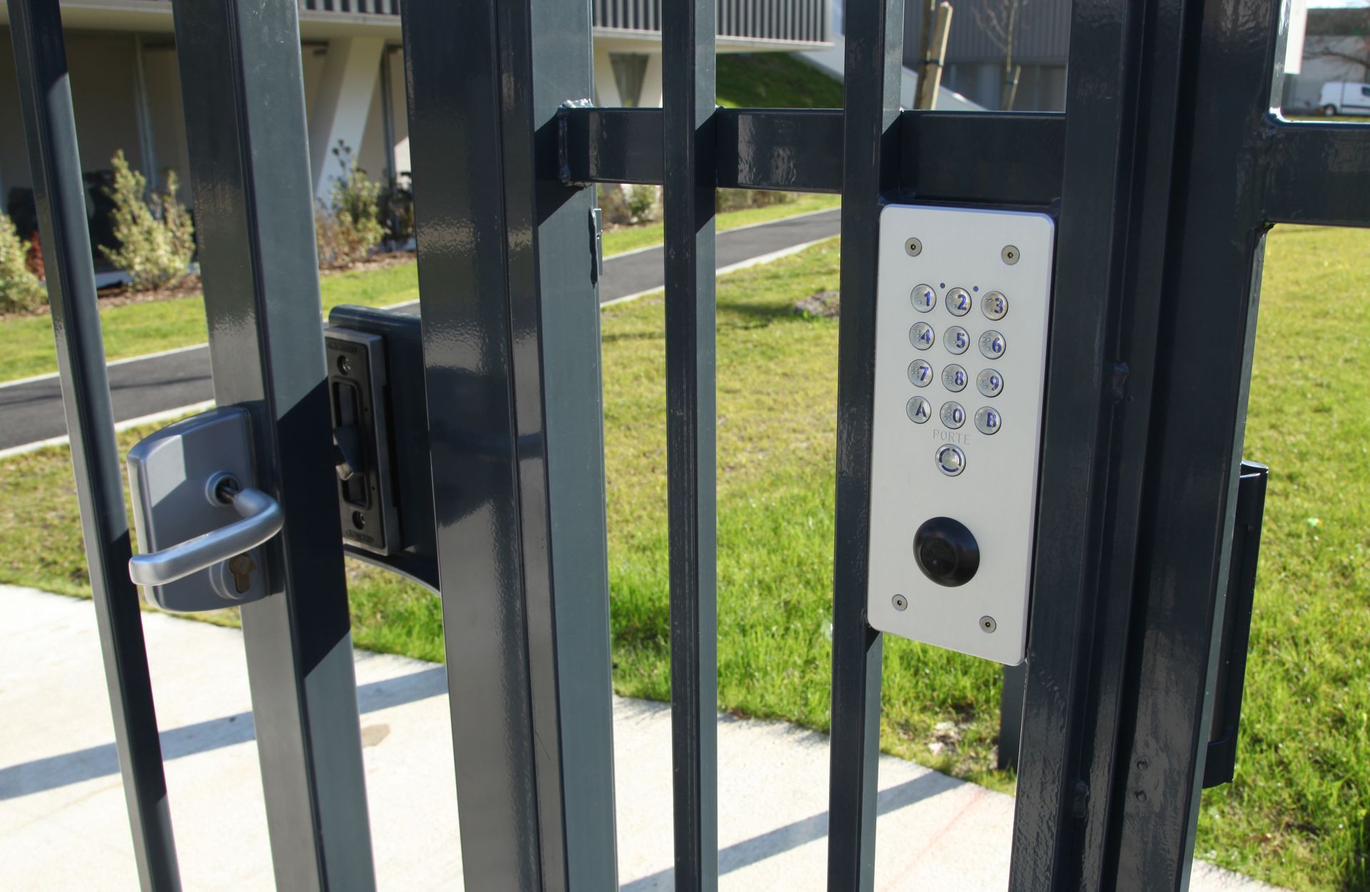 Portail en métal noir avec panneau d'entrée à clavier et loquet devant une maison.