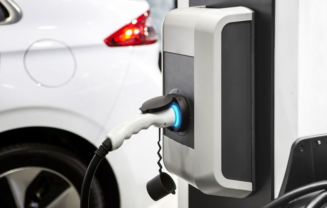 Voiture électrique en charge à une station, avec véhicule blanc et câble branché.