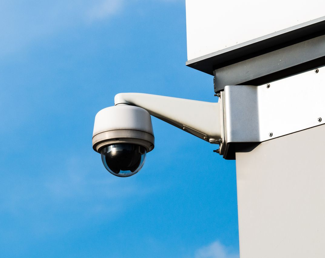 Caméra de sécurité extérieure fixée sur un bâtiment, pointant vers l'extérieur sur fond de ciel bleu