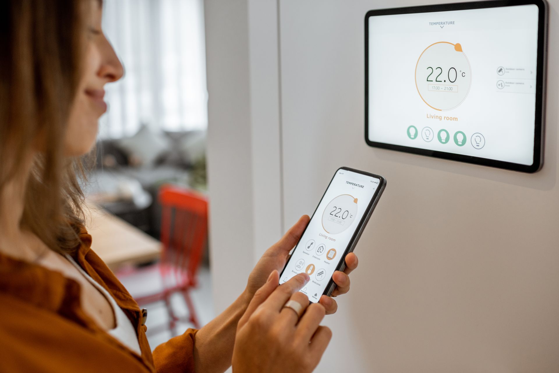 Une personne utilise un smartphone pour contrôler un thermostat intelligent mural dans une maison