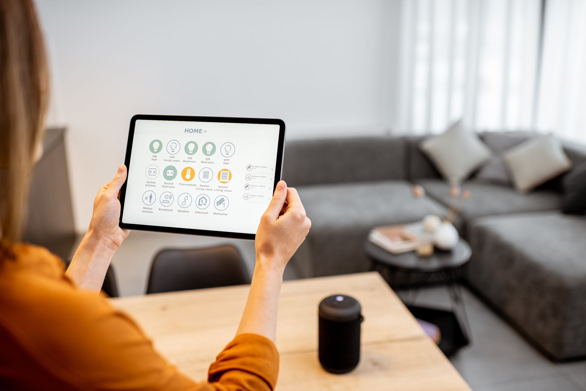 Une personne utilise une tablette dans un salon moderne, consultant un tableau de bord de maison connectée.