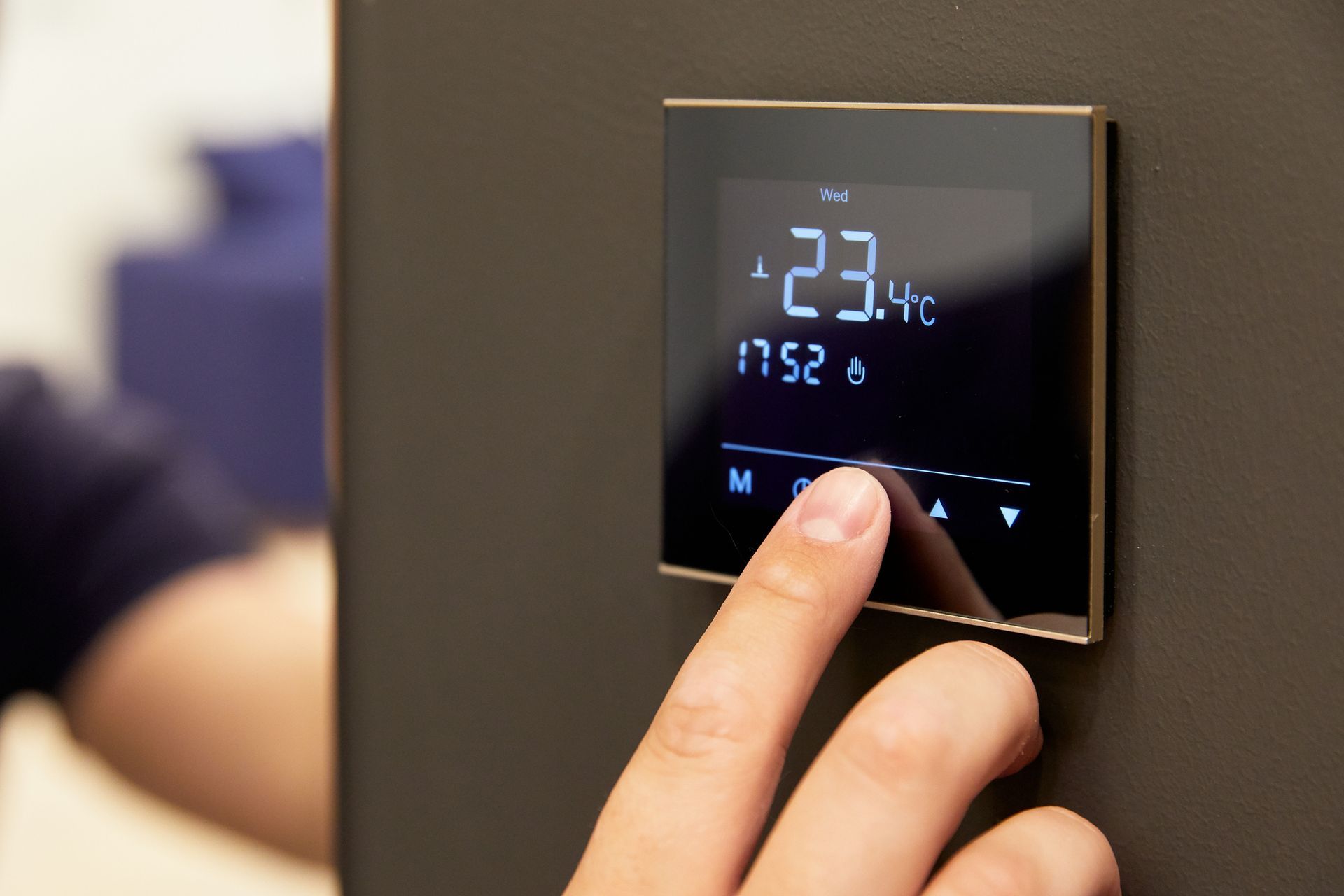 Une main touche un thermostat mural affichant 23 °C sur un écran noir à chiffres bleus