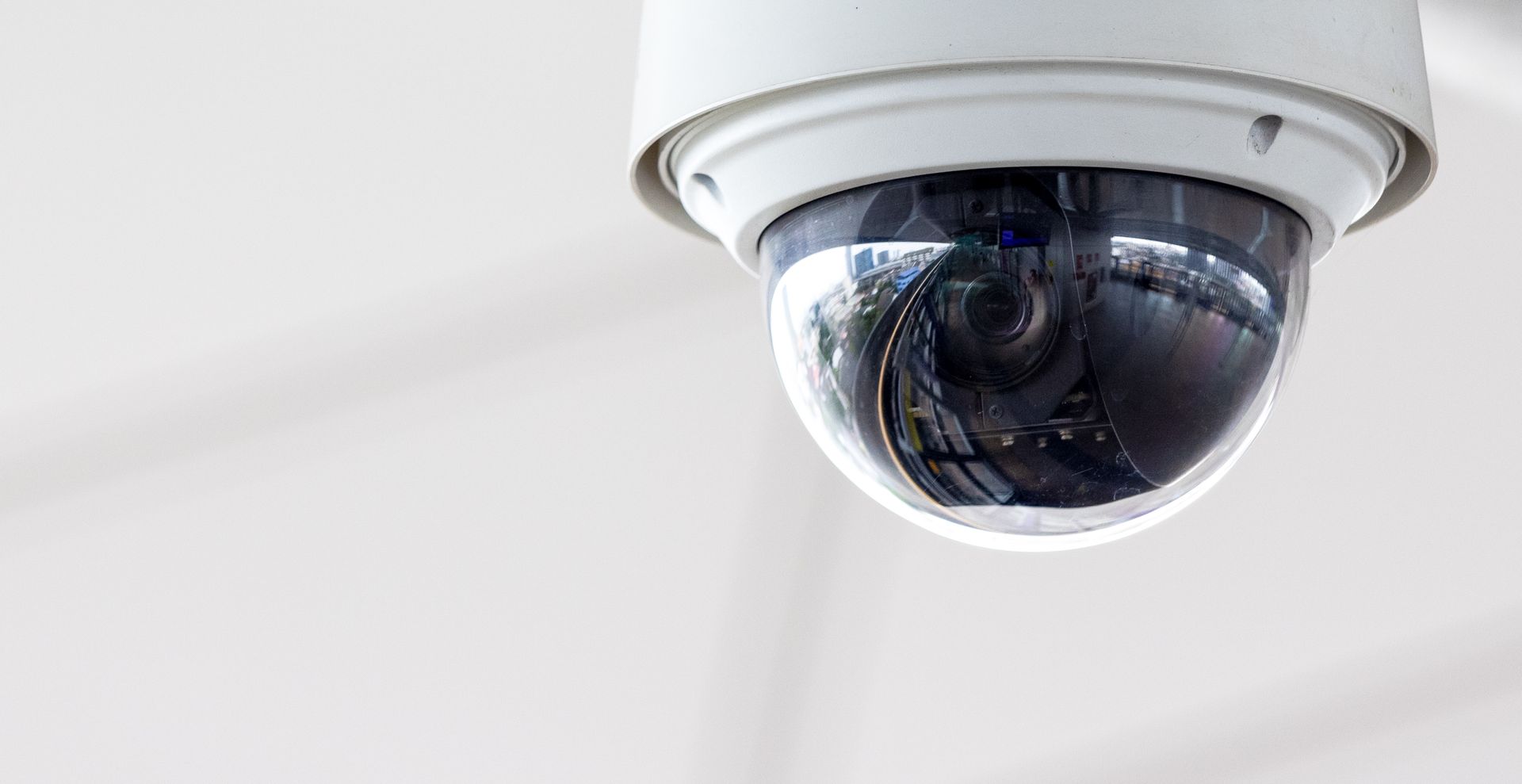 Caméra de sécurité dôme blanc fixée dans un angle du plafond, inclinée vers le bas