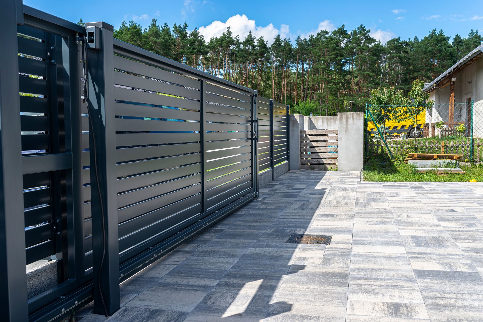 Portail et clôture modernes en métal noir le long d'une allée pavée, à côté d'une maison et d'un jardin.