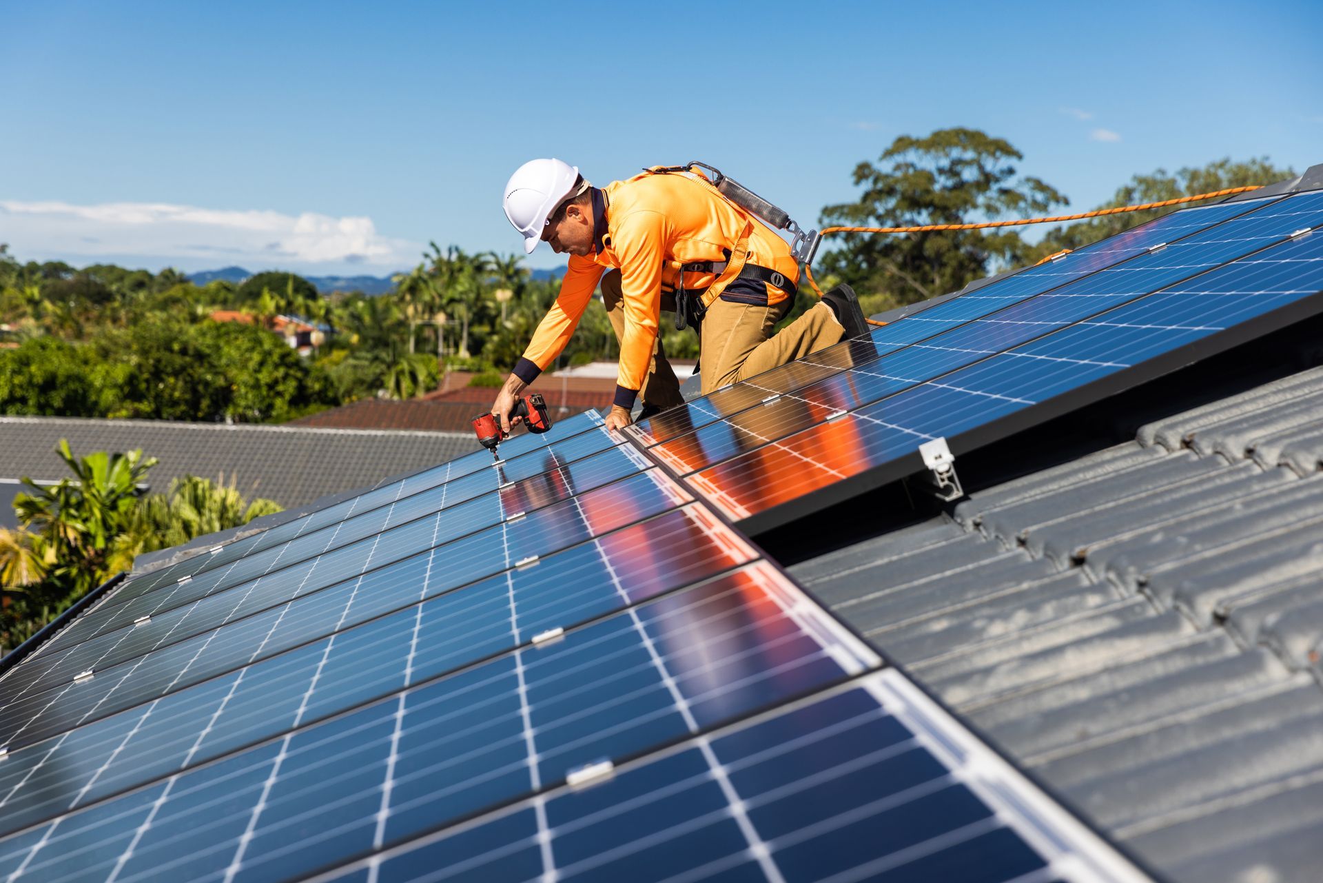 Un ouvrier installe des panneaux solaires sur un toit sous un ciel bleu dégagé.
