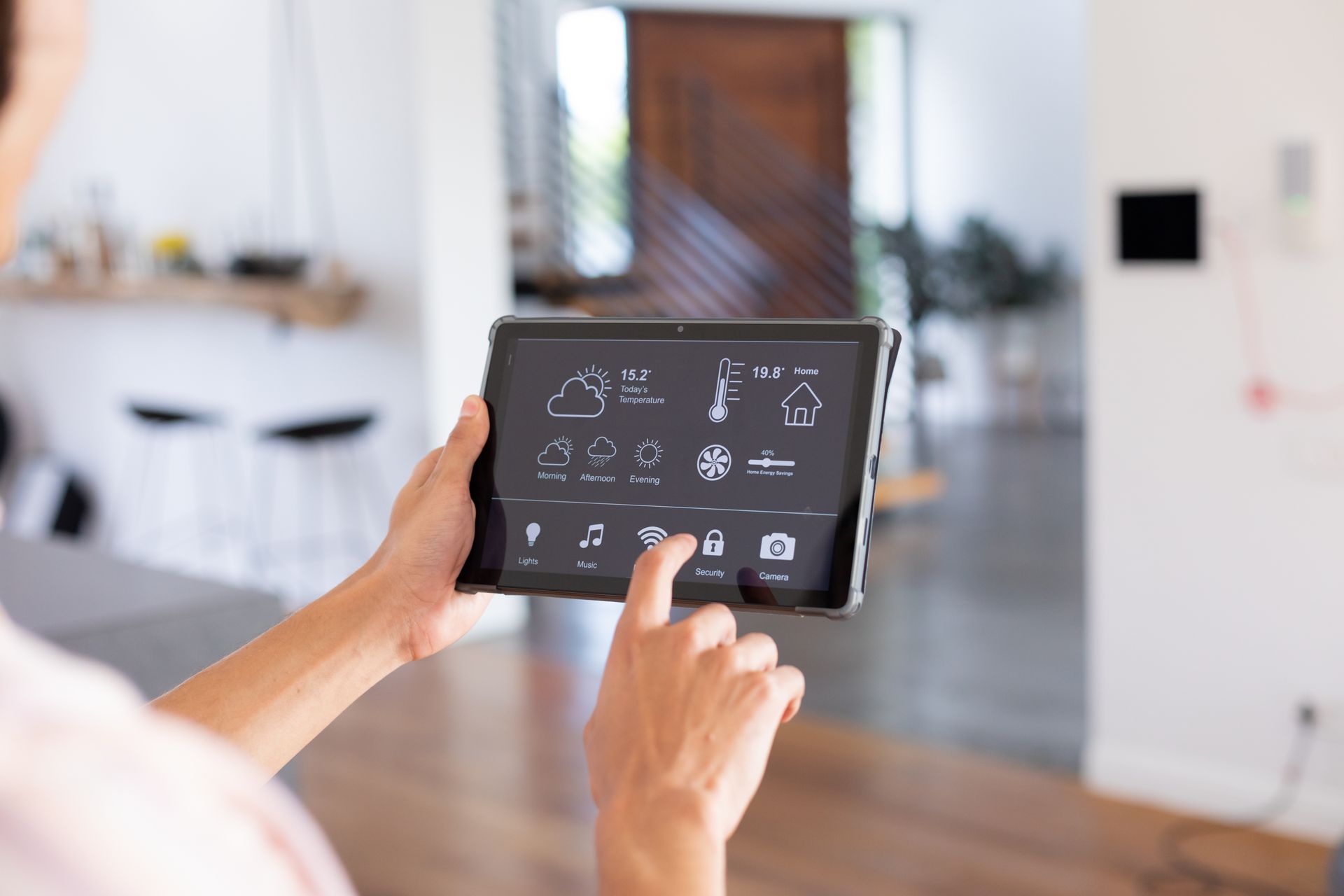 Des mains manipulent une tablette avec commandes domotiques dans un salon lumineux.