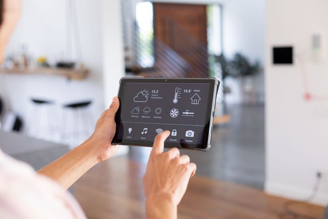 Une personne utilise une tablette pour contrôler un système domotique dans un salon lumineux.