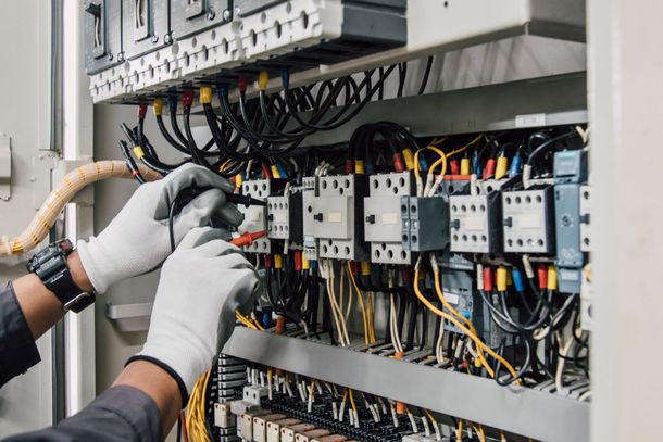Un technicien ganté effectue le câblage d'un panneau de commande électrique avec des câbles multicolores.