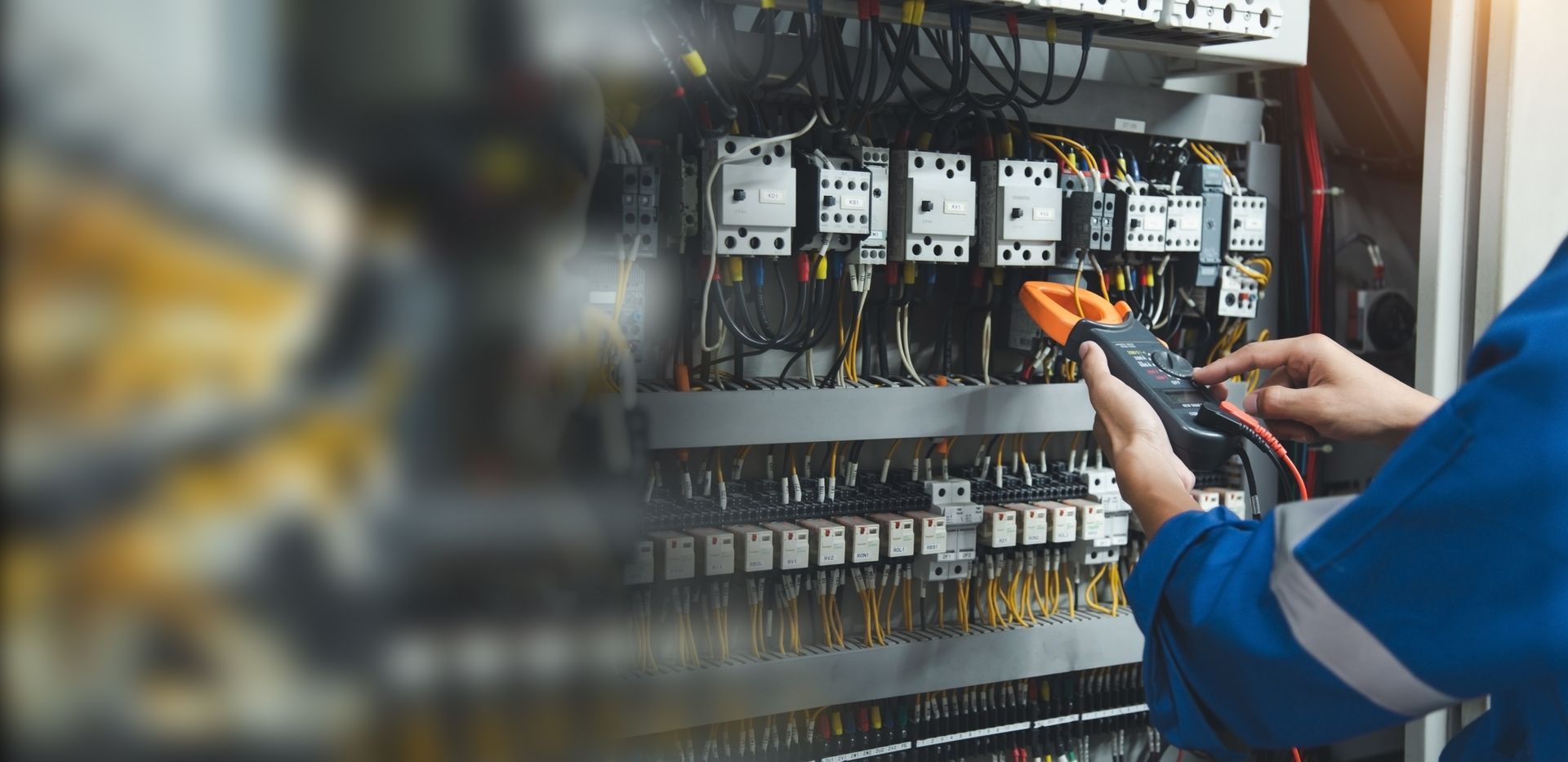 Un technicien teste le câblage d'un panneau de commande électrique à l'aide d'un multimètre.