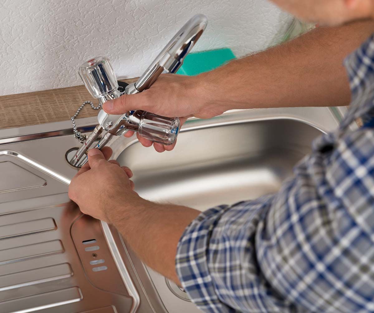 Un hombre está arreglando un grifo en un fregadero de cocina.
