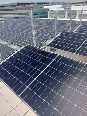 Un trabajador con equipo de protección y casco sostiene un taladro mientras está de pie junto a unos paneles solares en un campo al aire libre.