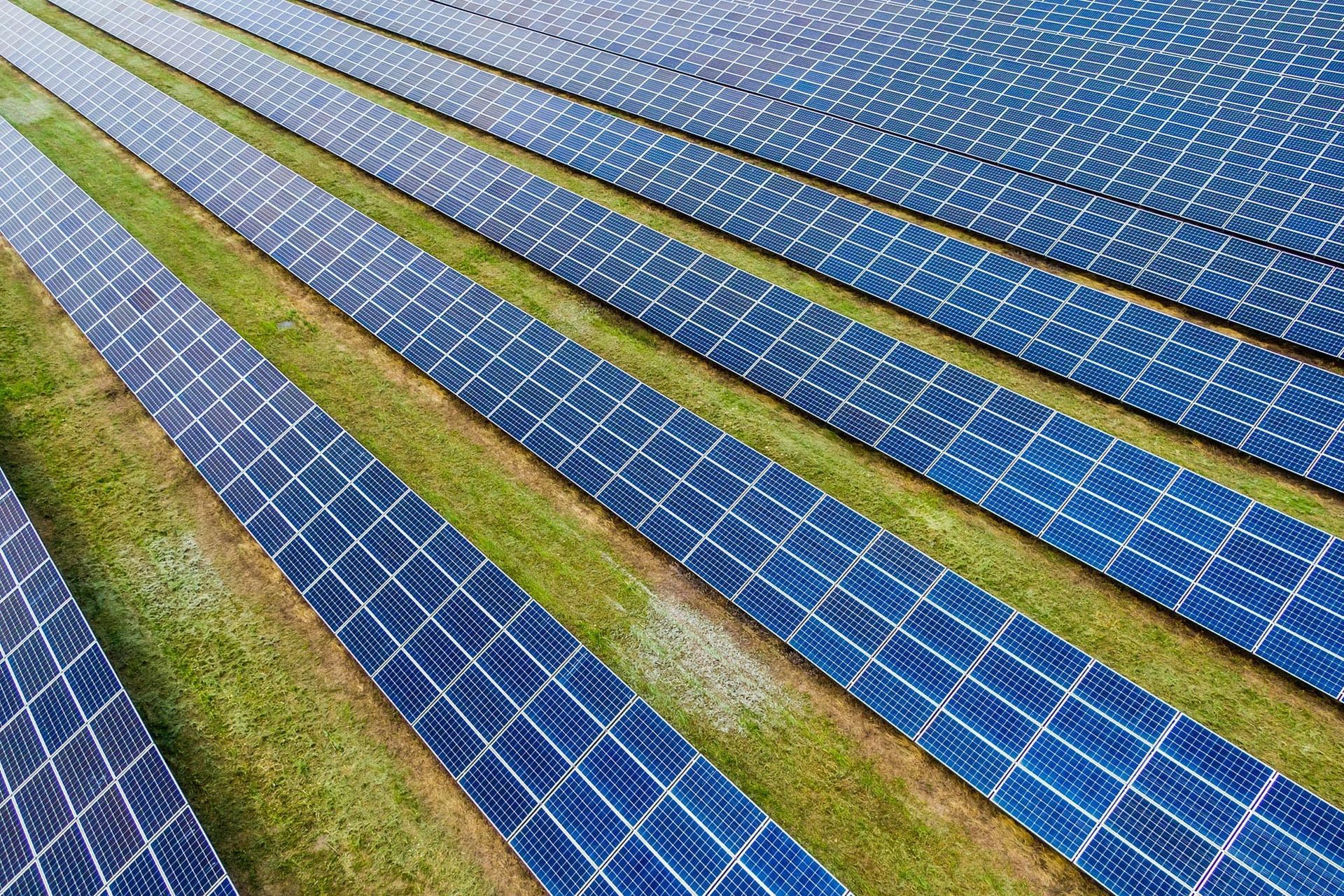 Dos trabajadores con equipo de seguridad limpian paneles solares con un pulverizador de agua y una escobilla de goma en un campo al aire libre.