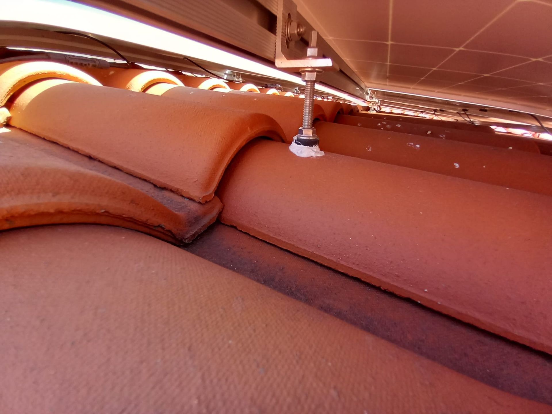 Un soporte metálico para paneles solares está fijado a un tejado de tejas de color terracota con un sellador alrededor de su base.