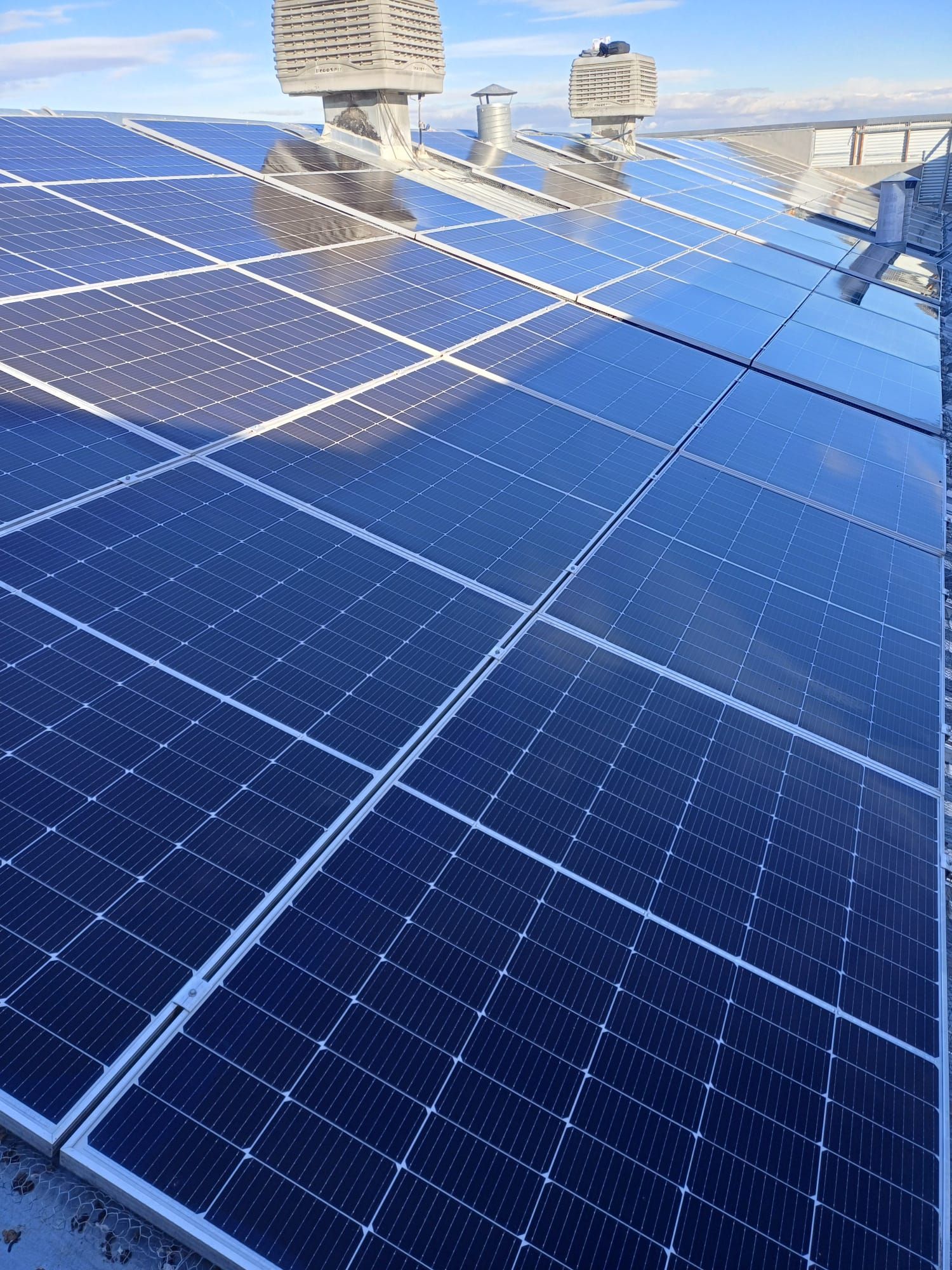 Vista desde un ángulo elevado de los paneles solares que cubren un tejado con dos chimeneas, con un cielo azul despejado de fondo.