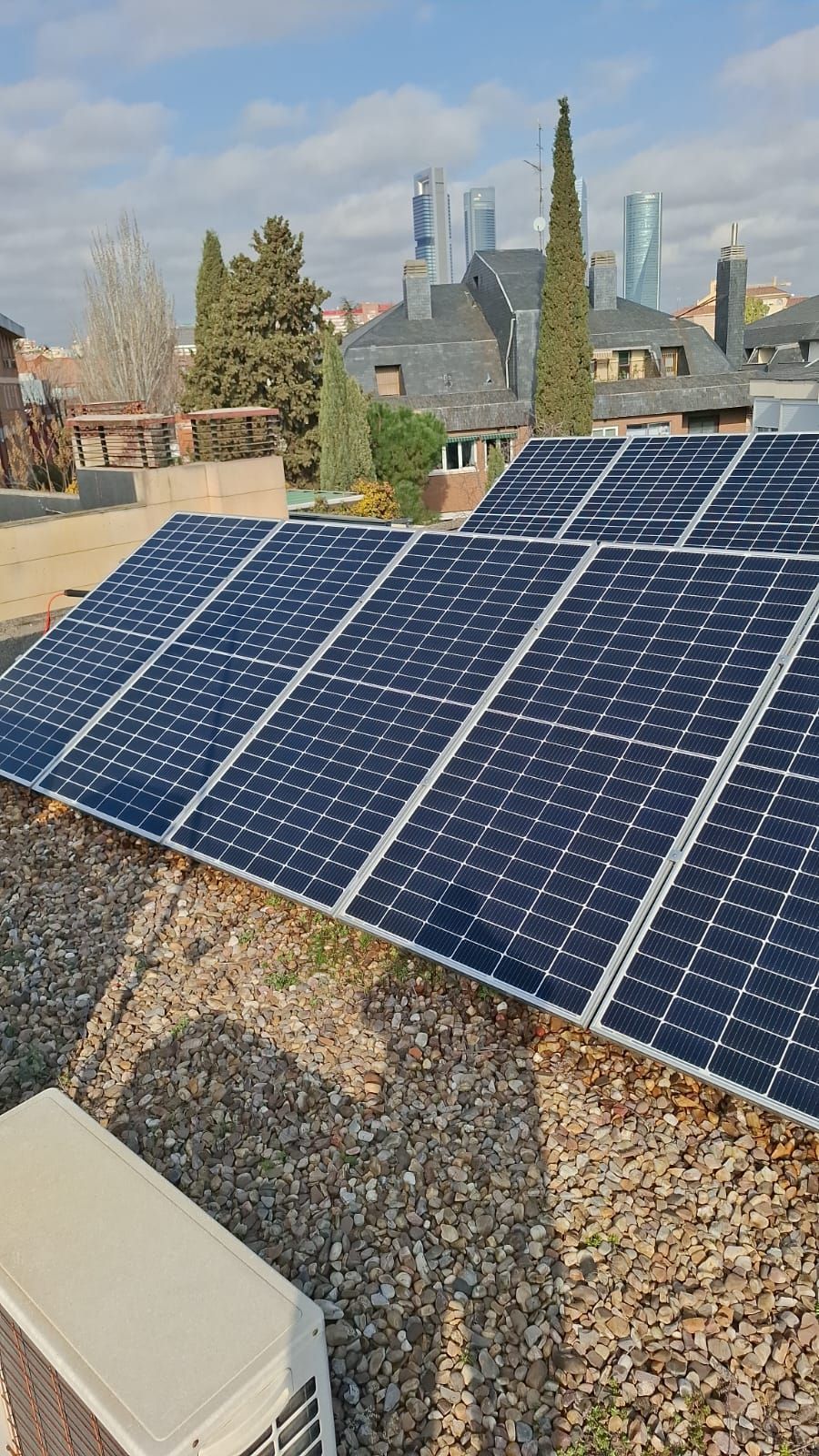 Paneles solares instalados en un tejado de grava, con un barrio residencial y edificios altos visibles al fondo.