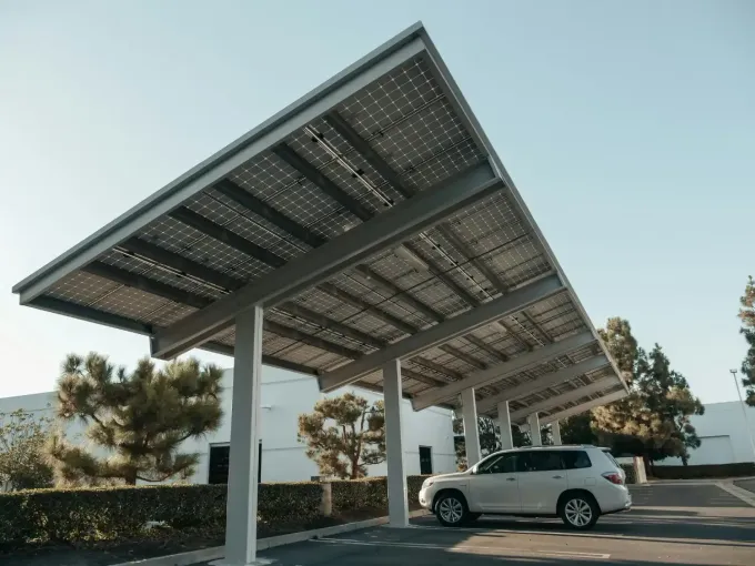 Cochera con paneles solares sobre una camioneta blanca estacionada. Vigas de acero, paneles y un soleado entorno exterior.