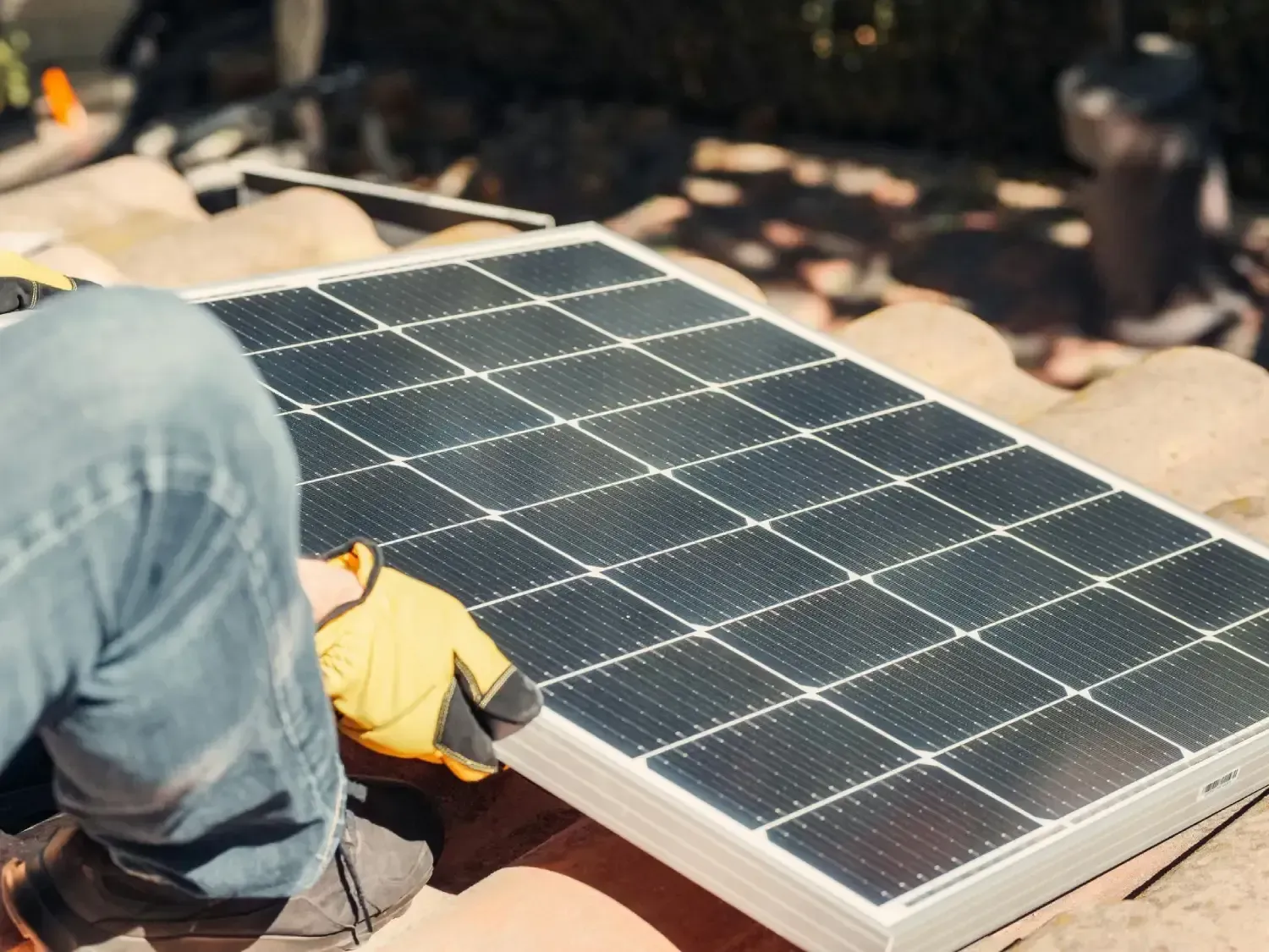 Una persona con guantes amarillos instala un panel solar en un techo de tejas.