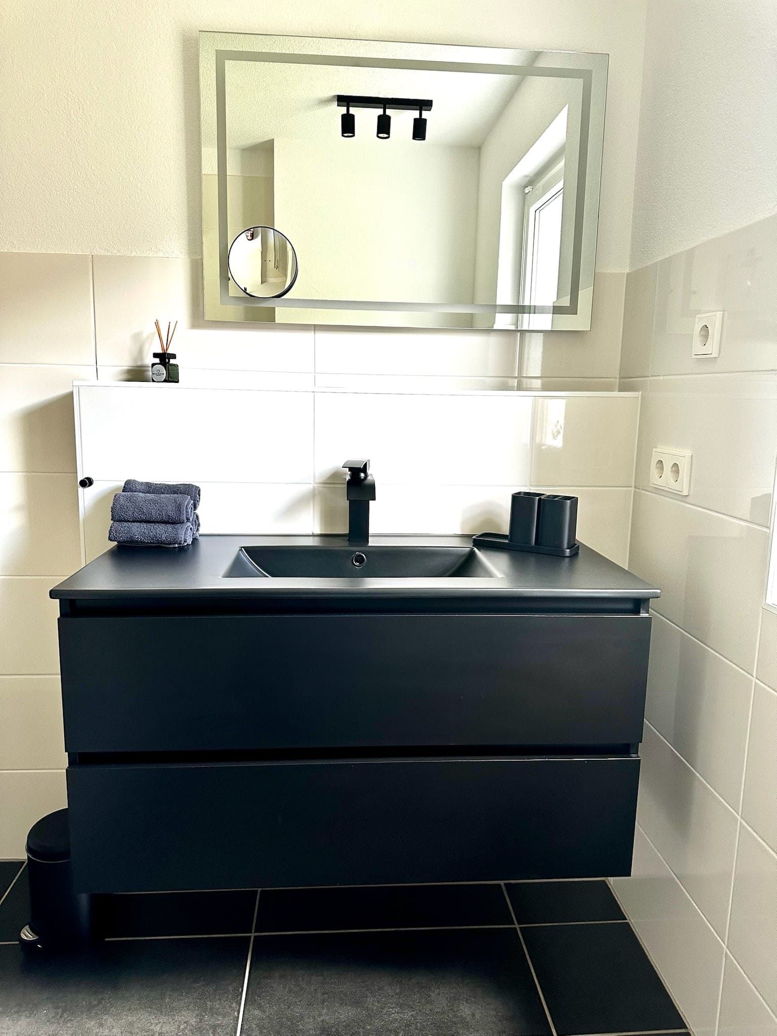 Modernes Badezimmer der Ferienwohnung in Feldberg mit schwarzem Waschtisch und beleuchtetem Spiegel