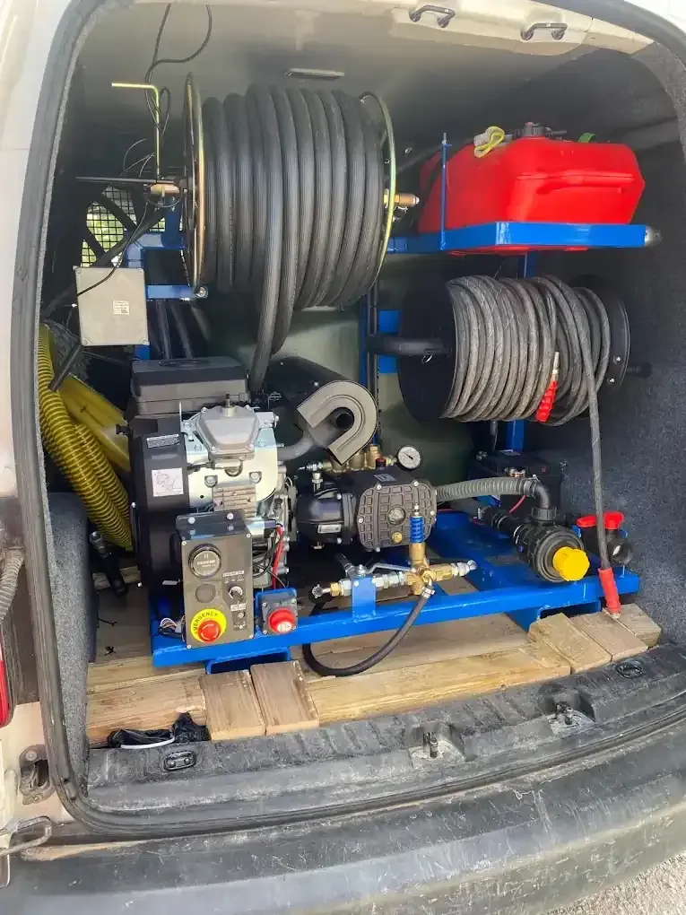 Una máquina de chorro de alta presión instalada en una furgoneta. Cuenta con un carrete de manguera, motor y tanques, todo montado sobre un bastidor azul.