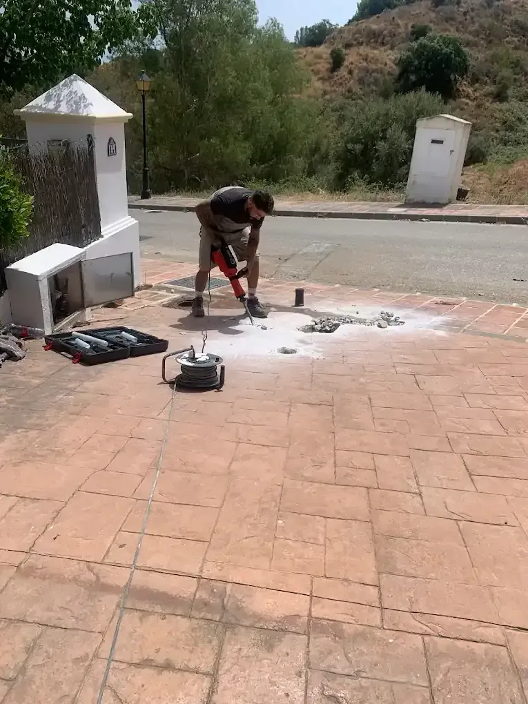Una persona que utiliza un martillo neumático para romper el pavimento al aire libre cerca de una pequeña estructura.