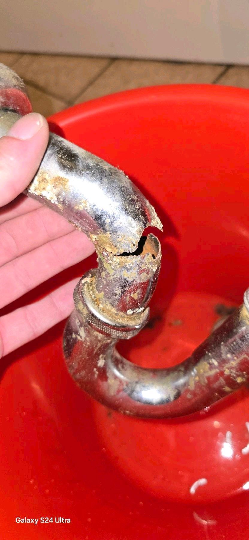 Eine Hand hält ein abgebrochenes, korrodiertes Chromrohrstück über einen roten Behälter.