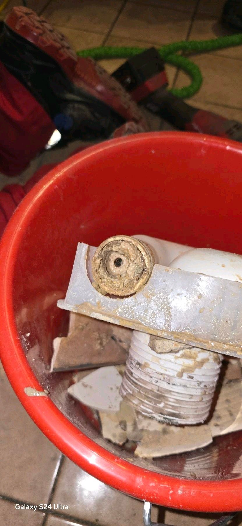 Ein roter Eimer mit Bauschutt, darunter ein runder Gegenstand mit einem Loch in der Mitte.