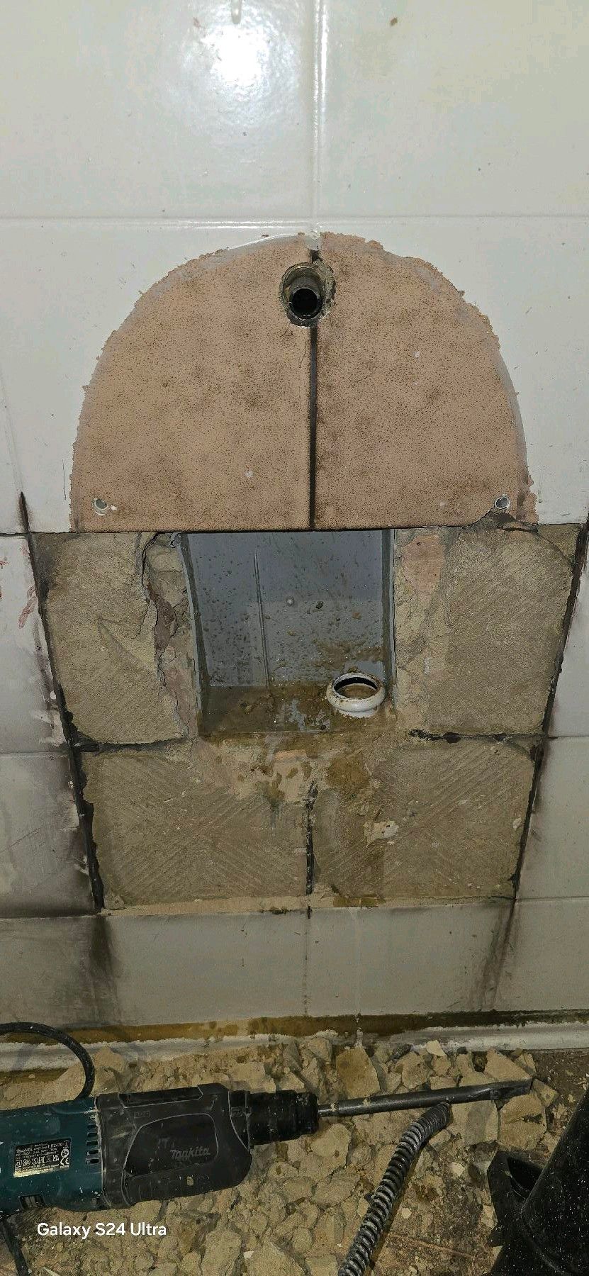 Bauarbeiten an einer Wand: Ein Loch mit einem Metallrohr und Betonblöcken. Unten befindet sich ein Bohrer.