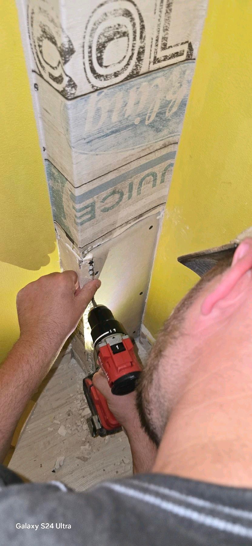 Person, die eine Bohrmaschine an einer weißen Säule in einem gelben Raum verwendet.