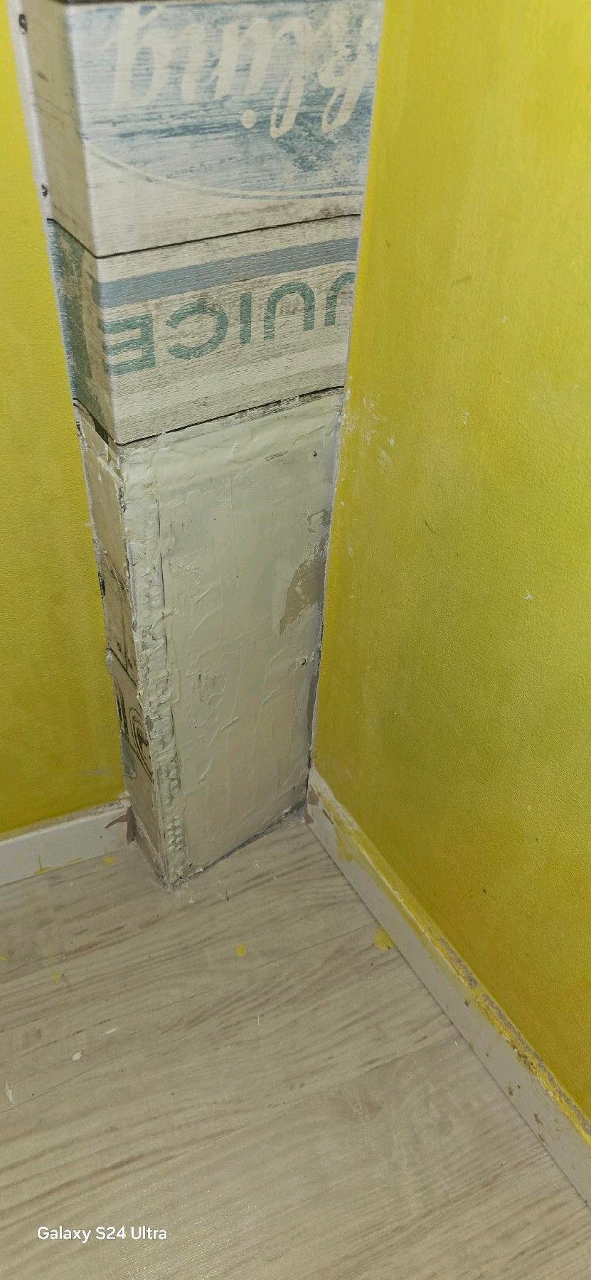 Eine Ecke in einem Raum mit einer Säule, die in eine Verpackung mit der Aufschrift „JUICE“ eingewickelt ist.