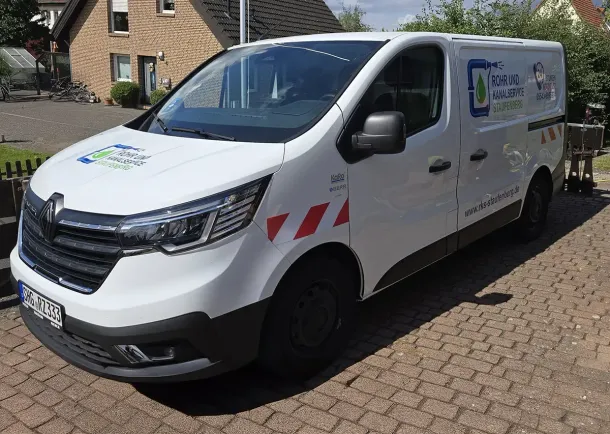 Weißer Renault-Transporter mit Firmenlogo auf Kopfsteinpflaster geparkt.