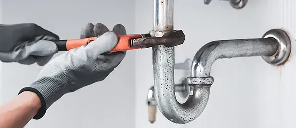 Klempner mit Handschuhen repariert mit einem Schraubenschlüssel ein Abflussrohr in einer weißen Umgebung.