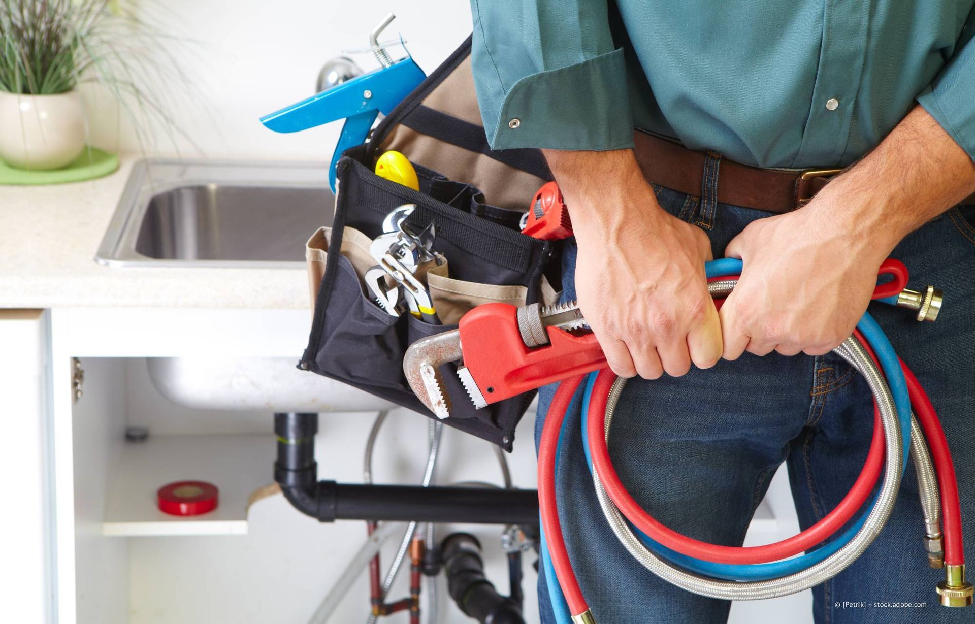 Ein Klempner mit Werkzeug und Schläuchen steht an einer Küchenspüle.