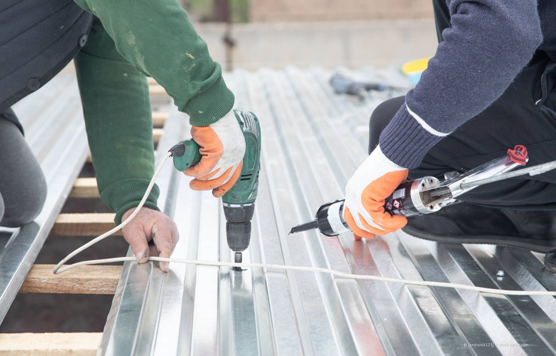 Zwei Personen montieren Metalldächer mit Hilfe einer Bohrmaschine und einer Kartuschenpistole.