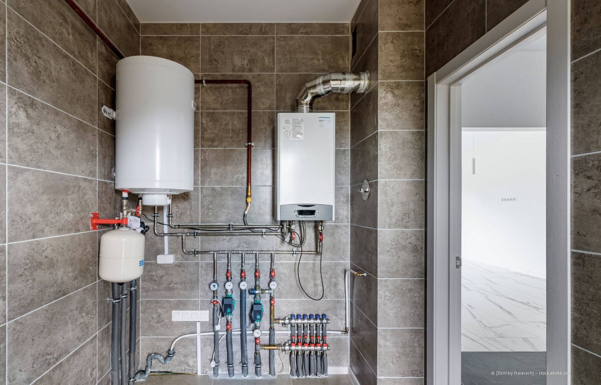 Warmwasserbereiter und Boiler an gefliester Wand in einem Hauswirtschaftsraum, Tür rechts.