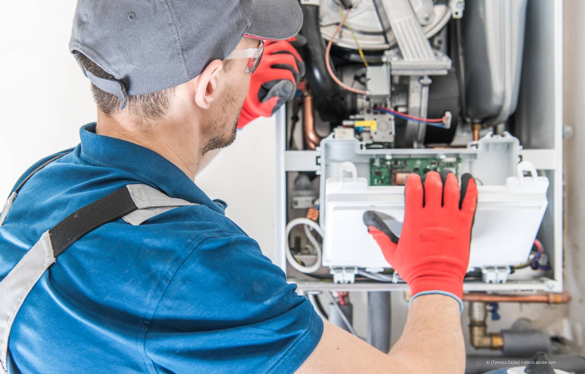 Eine Person in blauem Hemd und Handschuhen untersucht ein weißes Haushaltsgerät.