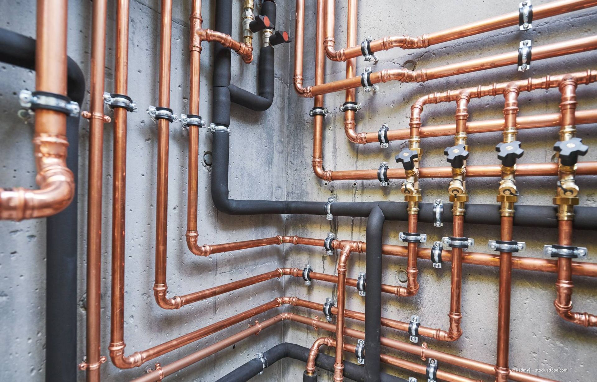 Kupferrohre und schwarz isolierte Rohre sind an einer Betonwand befestigt.