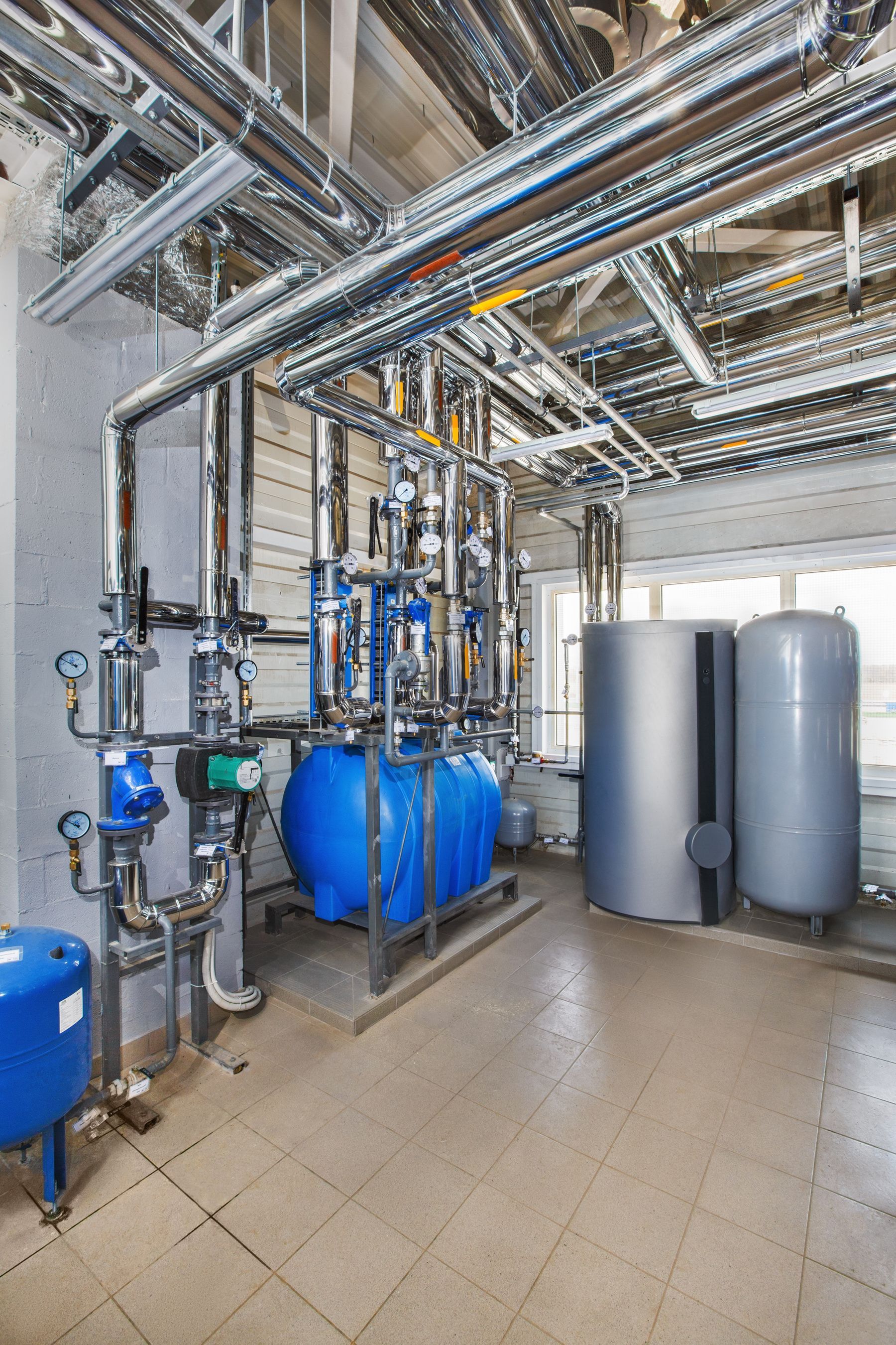 Salle de traitement des eaux industrielles avec réservoirs bleus, tuyaux et filtres cylindriques.