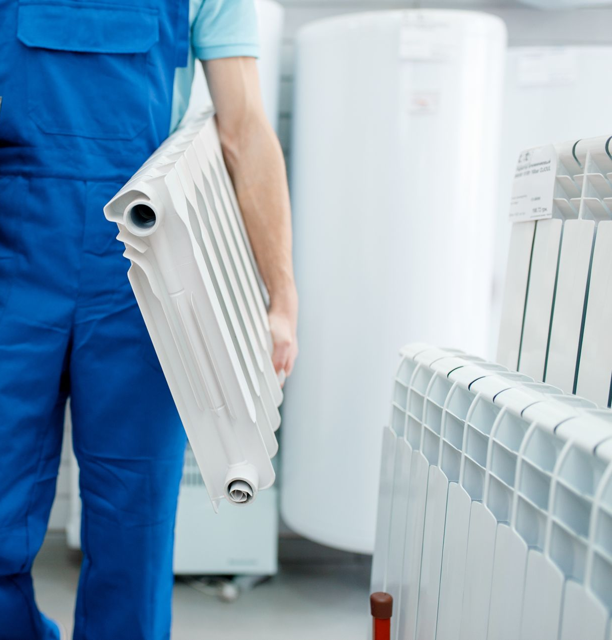 Ouvrier en salopette bleue transportant un radiateur blanc