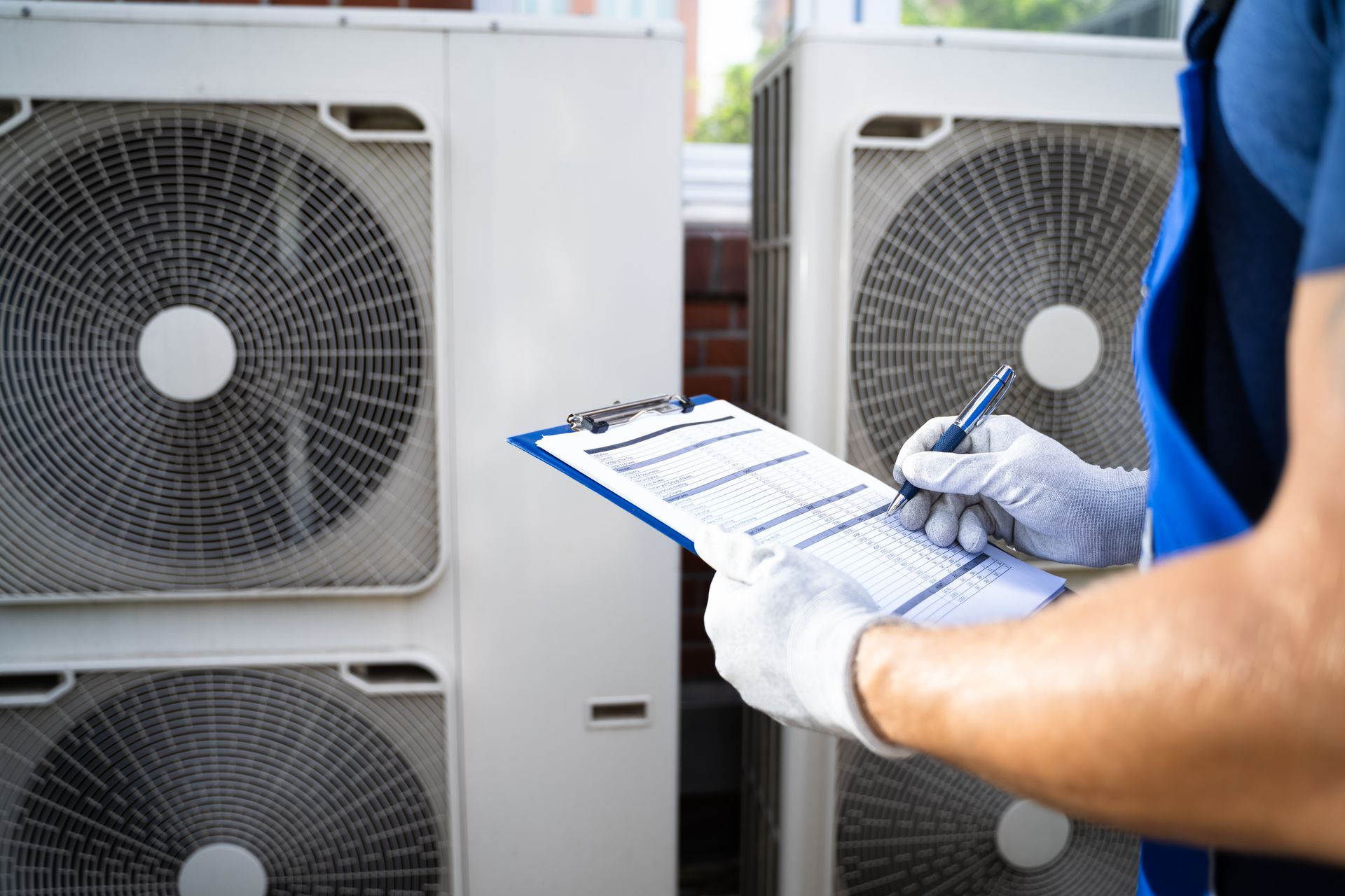 Un technicien inspecte des unités de climatisation extérieures à l'aide d'un bloc-notes.
