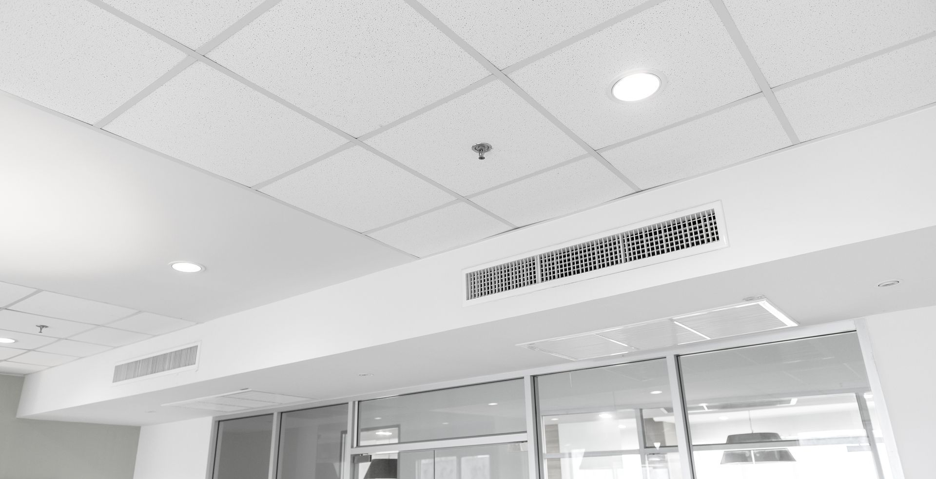 Plafond de bureau blanc éclatant avec spots encastrés et bouches d'aération.