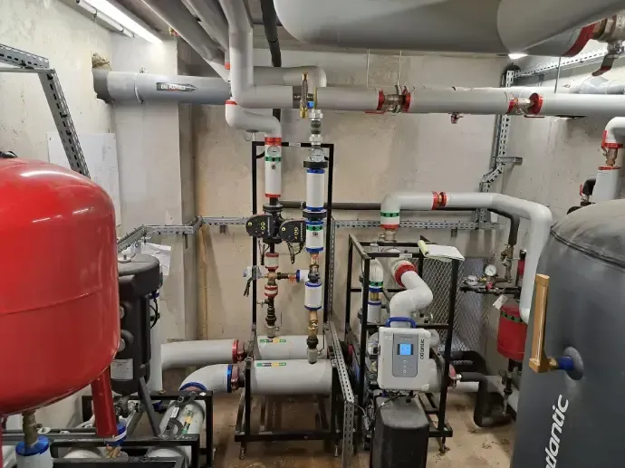 Local technique avec pompes, tuyaux et un réservoir sous pression rouge.