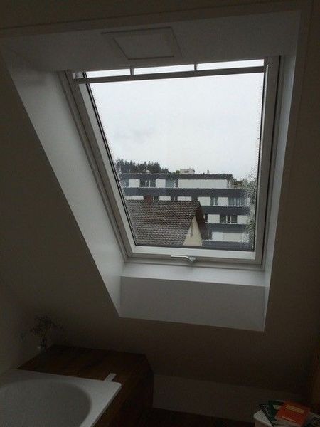 Oberlichtfenster in einer schrägen weißen Decke mit Blick auf ein Gebäude.