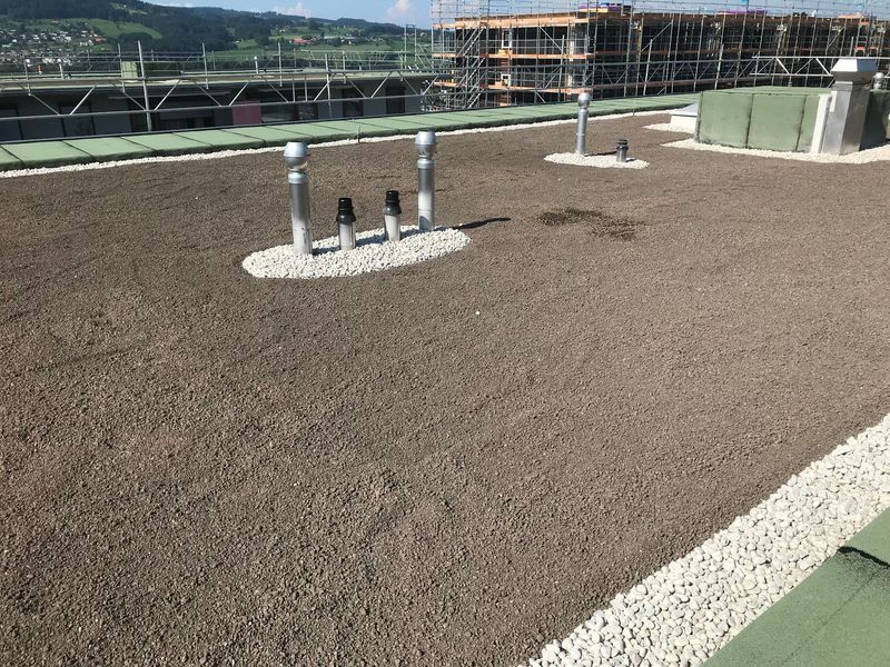 Kiesdach mit Rohren, umgeben von weißen Steinen, in einer städtischen Umgebung im Bau.