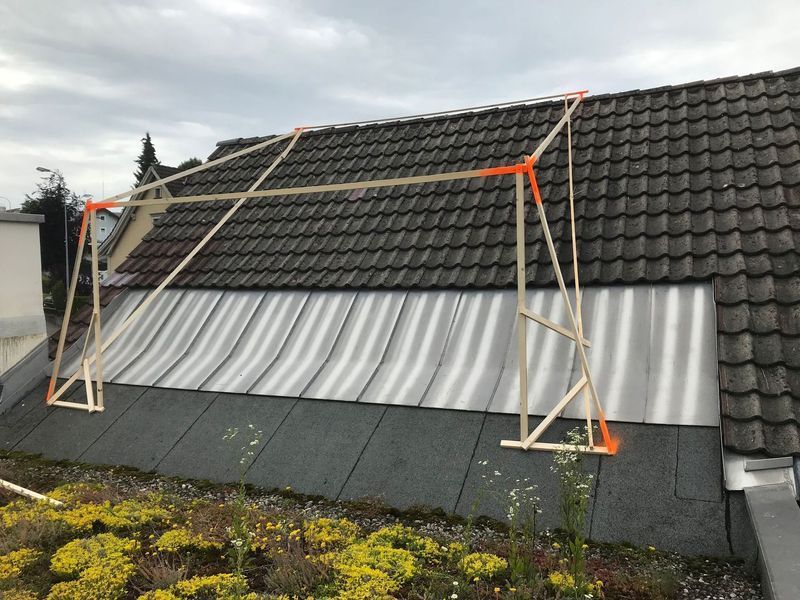 Holzrahmen mit orangefarbenen Verbindungsstücken, der auf einem schrägen Dach aufgestellt ist, wahrscheinlich für den Bau.