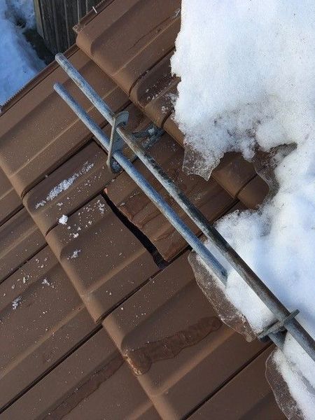 Metallischer Schneefang auf einem braunen Ziegeldach mit Schnee- und Eisansammlungen.