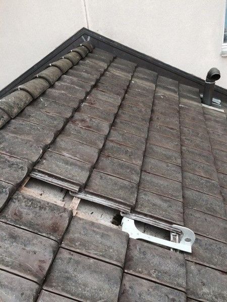 Ein Dach mit beschädigten Ziegeln, das in der Nähe der Kante eine offene Entlüftung aufweist.