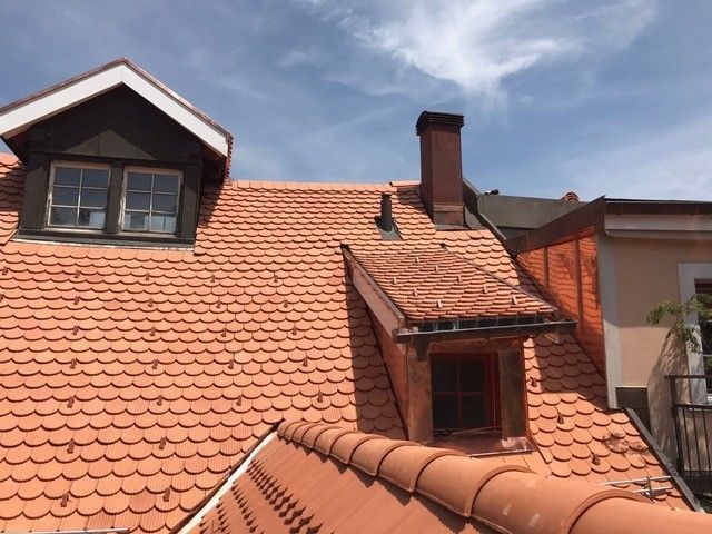 Orangefarbenes Ziegeldach mit Dachgauben und einem Schornstein vor blauem Himmel.