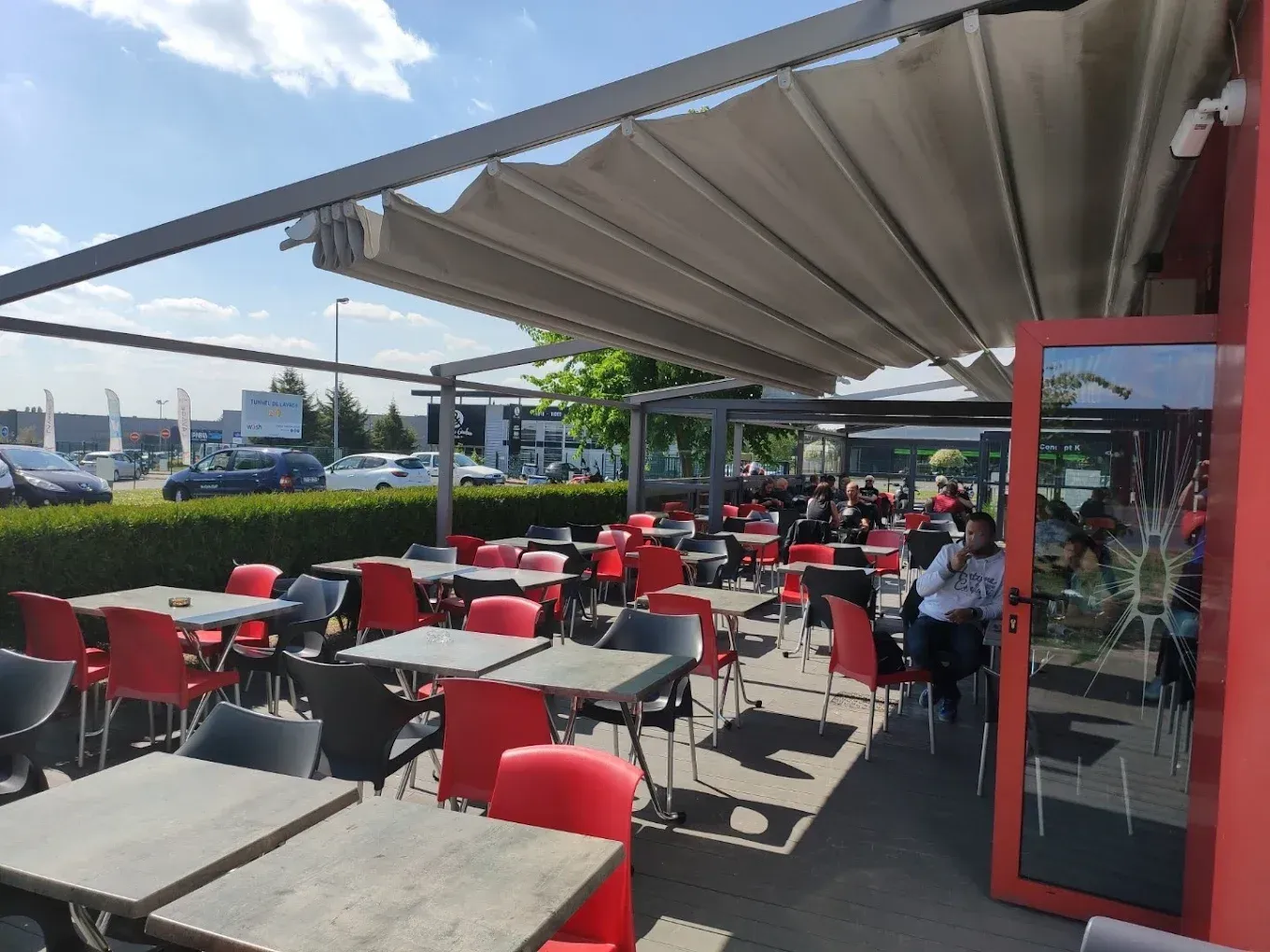 Terrasse de restaurant avec chaises et tables rouges et noires et auvent rétractable.