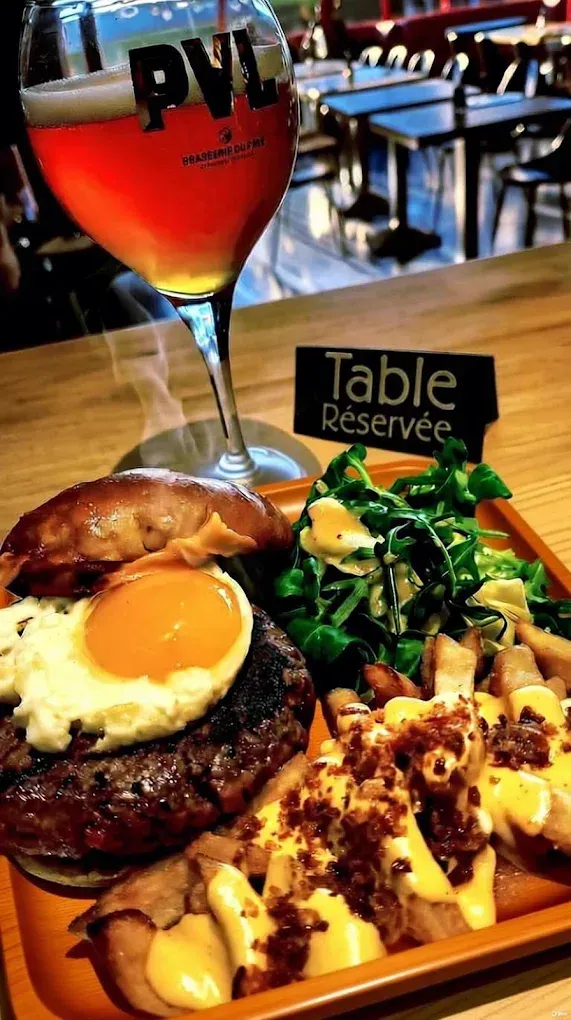 Burger avec œuf, frites, salade et bière sur un plateau en bois dans un restaurant.