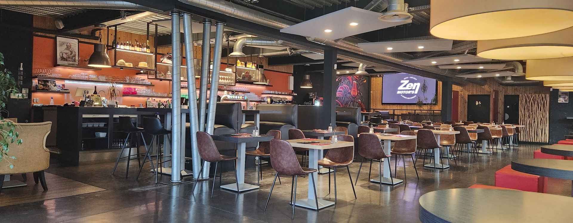 Intérieur d'un restaurant avec tables, chaises, bar et grand écran.